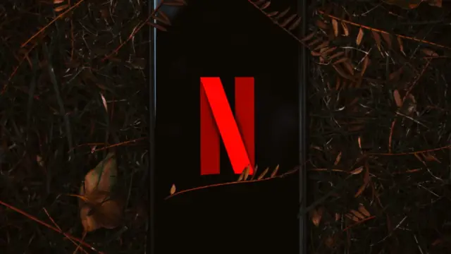 Smartfon z logo Netflix na ekranie leży na suchych liściach
