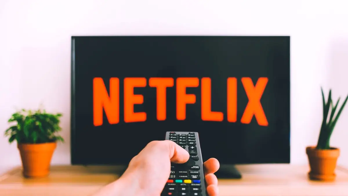 Dłoń z pilotem przed telewizorem z otwartym Netflixem
