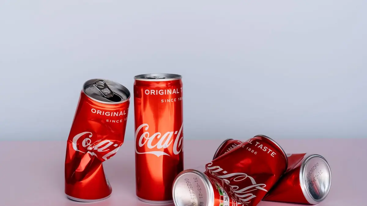 Puszki Coca-Coli ułożone na jasnym, pastelowym tle