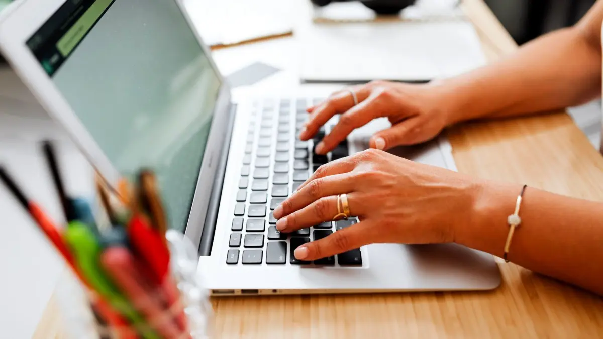 Osoba pisze na laptopie przy drewnianym biurku