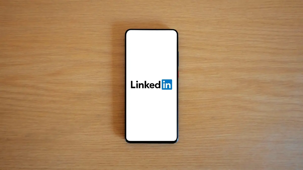 Smartfon z logo LinkedIna leży na drewnianym blacie