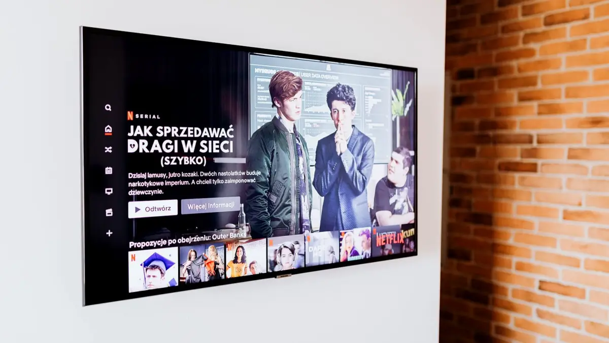 Telewizor w salonie z ceglaną ścianą wyświetla menu z filmami i programami
