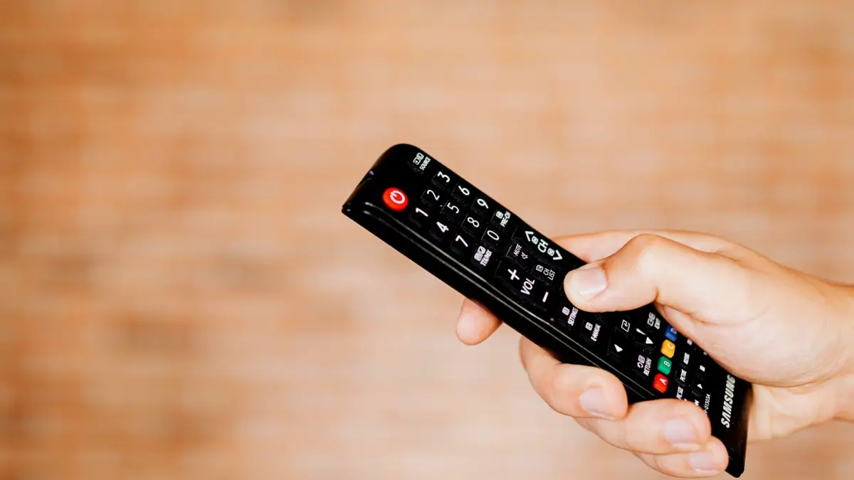 Dłoń trzymająca pilot do telewizora na jasnym, rozmytym tle