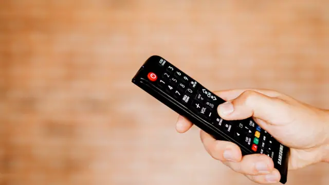Dłoń trzymająca pilot do telewizora na jasnym, rozmytym tle