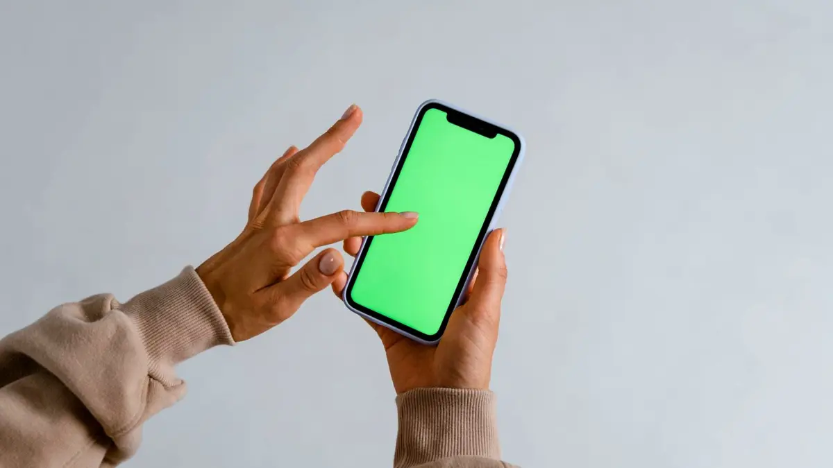 Dłonie trzymają smartfon z zielonym ekranem.