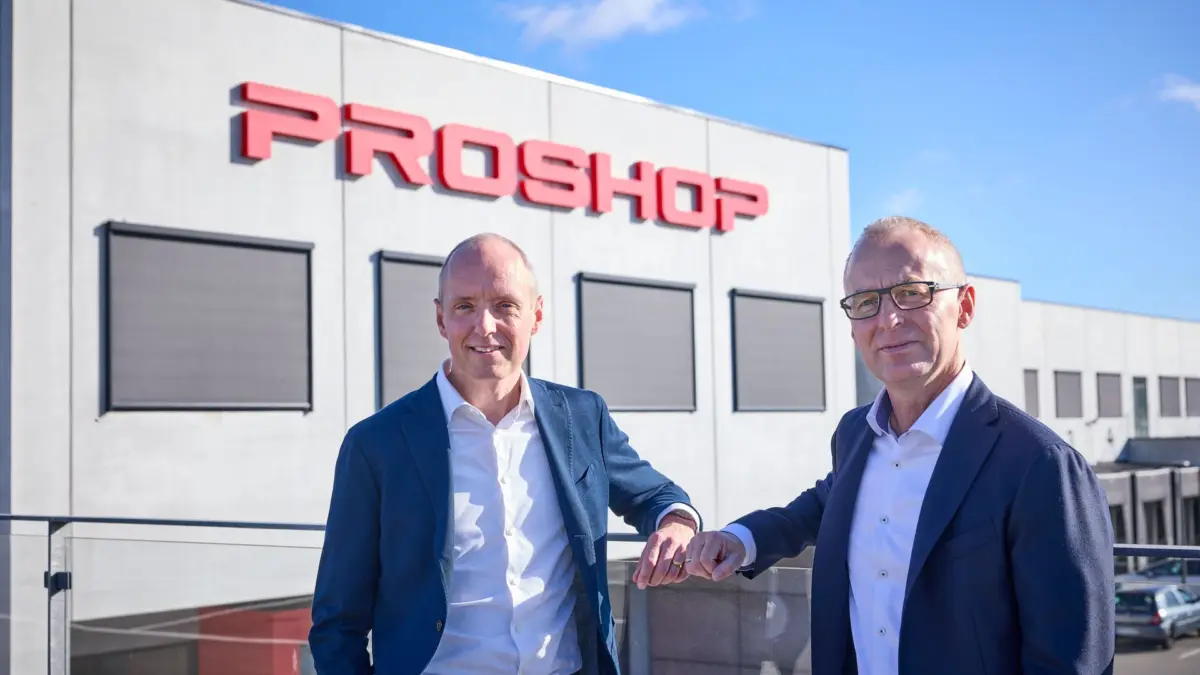 Dwóch mężczyzn w garniturach przed budynkiem z dużym czerwonym napisem Proshop