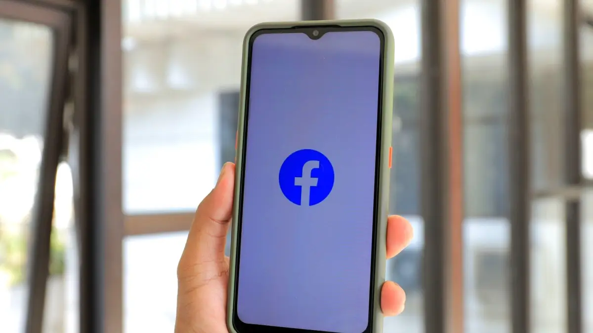 Dłoń trzyma smartfon z otwartą aplikacją Facebook